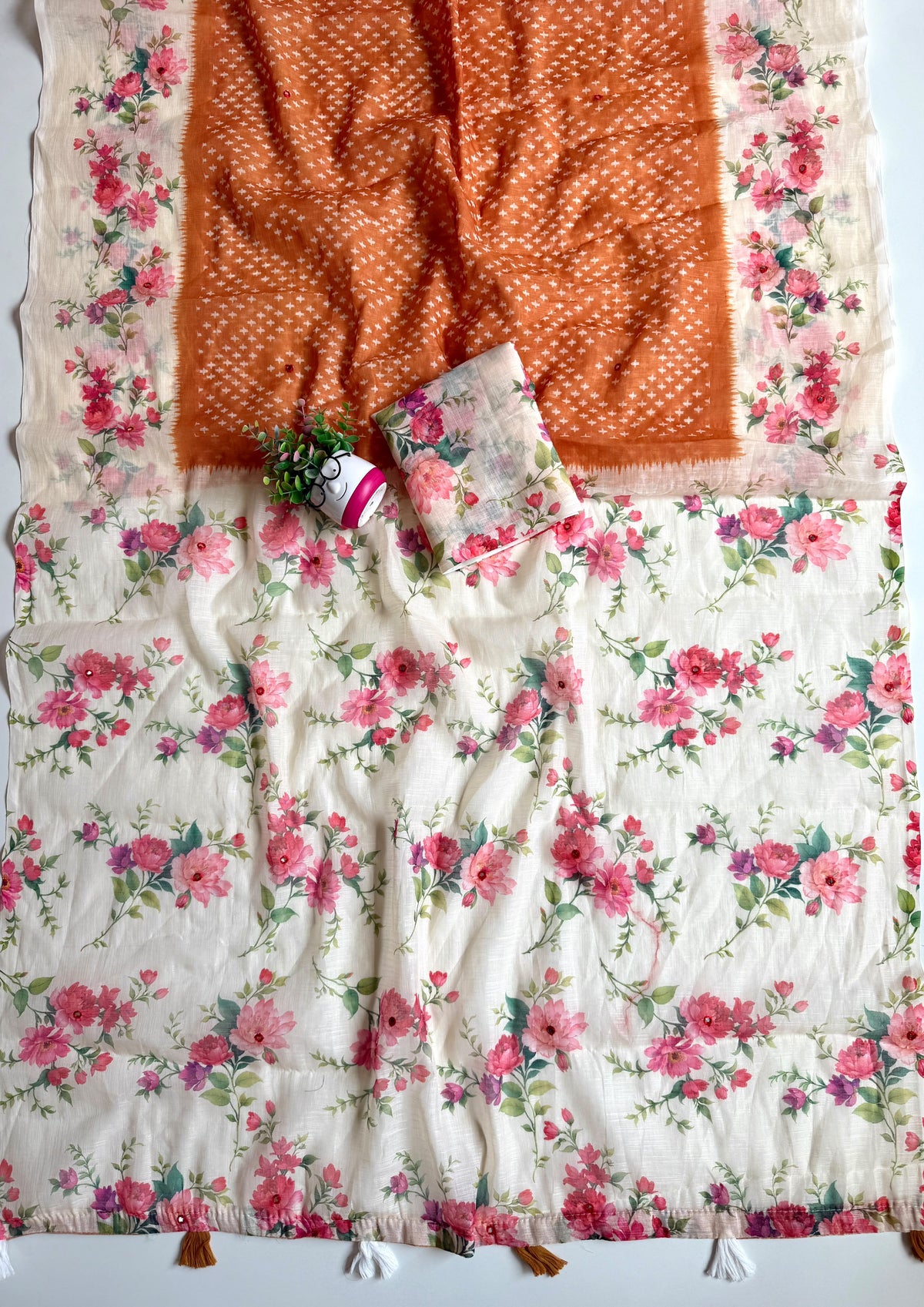 Rust orange linen cotton saree spread out showing cream floral pallu with mirror work and rust and white tassels