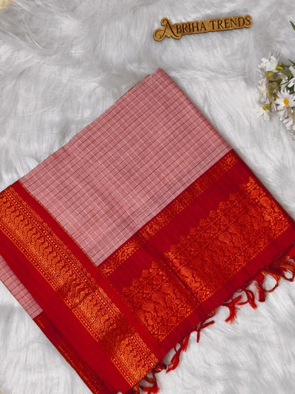 A folded red and pink saree with a pink checkered body, a rich red border, and an ornate gold zari brocade, displayed on a white faux fur background with a small gold 'Abhija Trends' logo and white flowers.