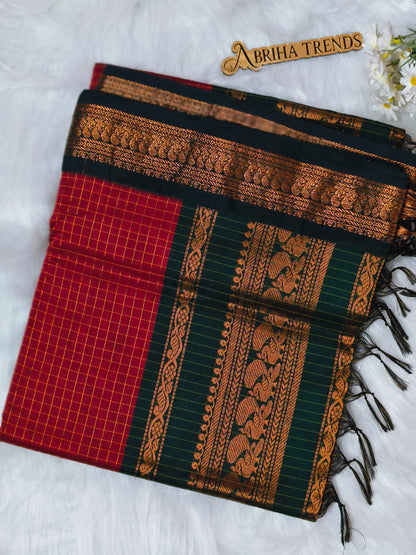 A folded traditional Indian saree with a red body, dark green border, and intricate gold zari embroidery, displayed on a white textured background with a decorative brand tag reading 'Abriha Trends'.