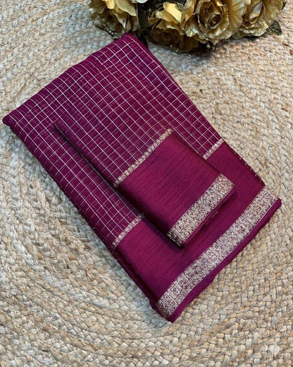 Folded purple fabric with white checkered pattern on a textured beige surface.