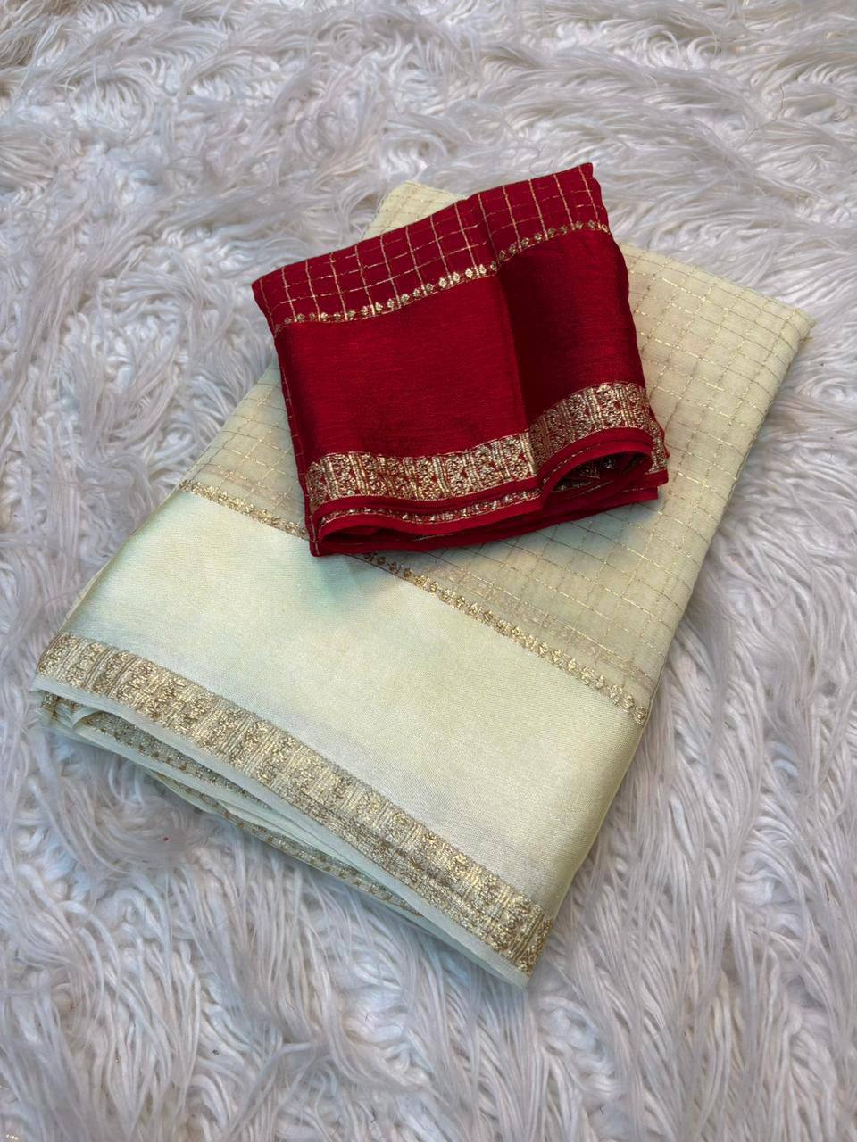 Red and gold saree on a light green fabric with gold border on a textured white background