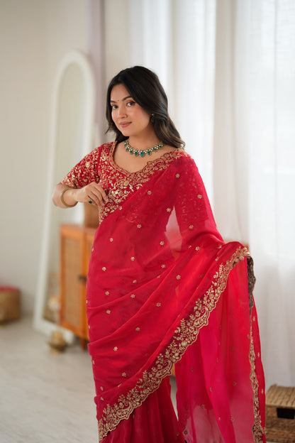 A woman wearing a bright red saree with gold embroidery and a matching embroidered blouse.