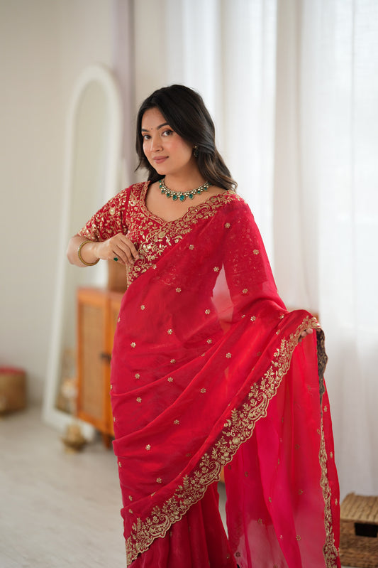 A woman wearing a bright red saree with gold embroidery and a matching embroidered blouse.