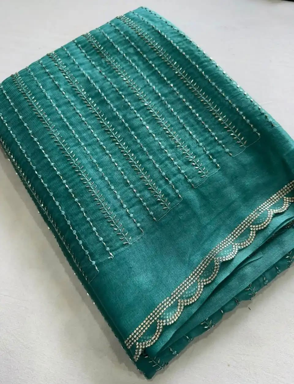 A folded teal green fabric piece, likely a dupatta or sari, featuring vertical rows of metallic silver embroidery and a scalloped border embellished with small silver beads, laid flat on a light surface.