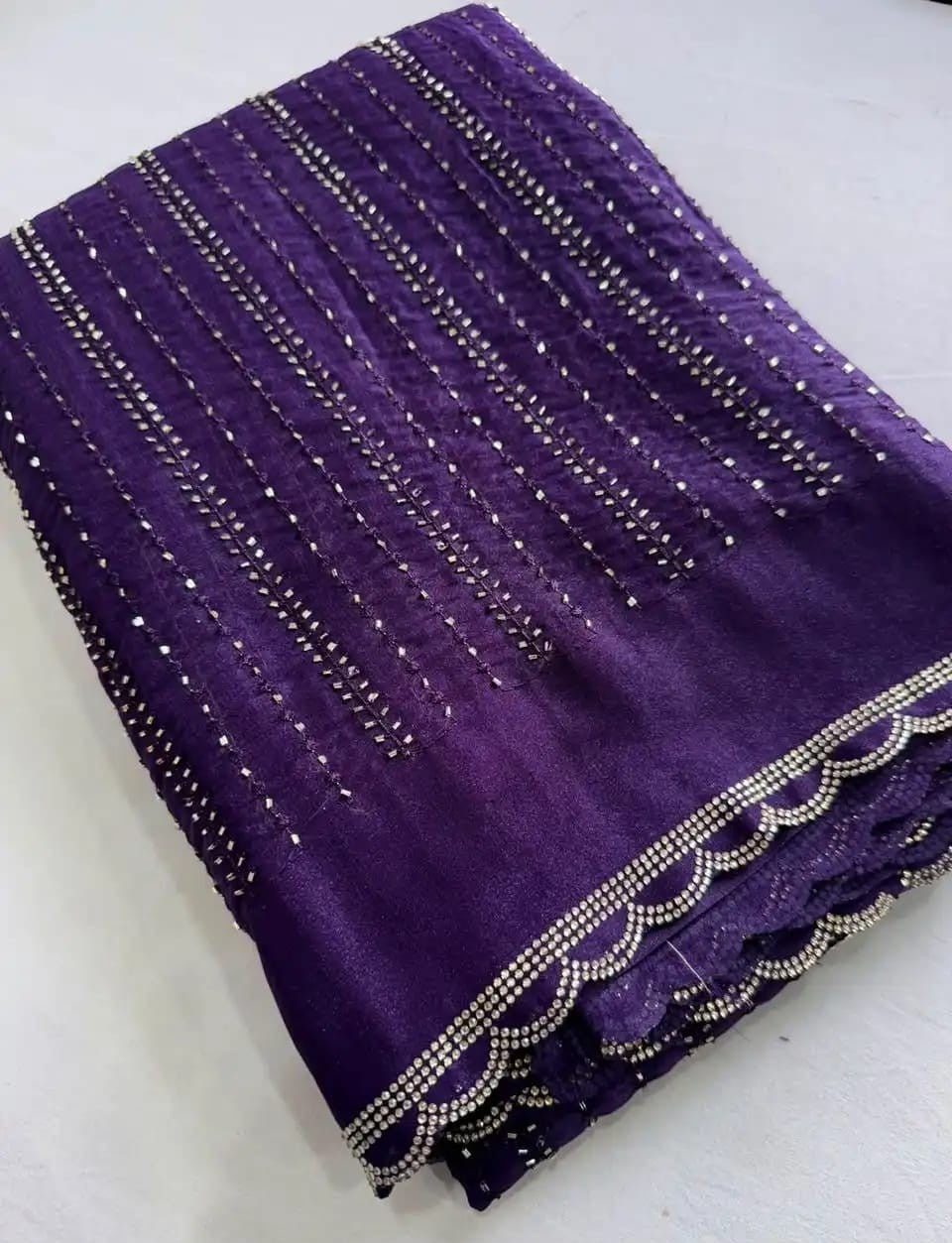 A folded purple fabric piece with vertical rows of silver bead embellishments and a scalloped beaded border, laid flat on a light surface.
