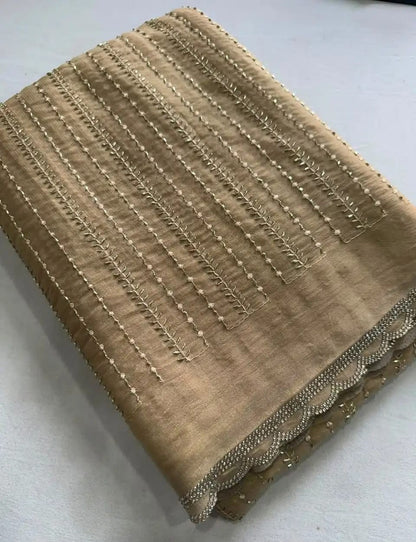 A folded beige fabric piece with vertical metallic gold embroidery and a scalloped embroidered border, shown on a light neutral background.