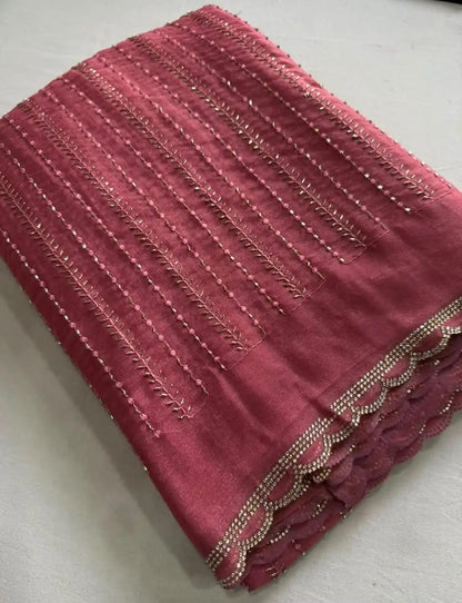 A folded piece of dusty rose pink fabric with vertical metallic gold embroidery and a scalloped beaded border, displayed on a light gray surface.