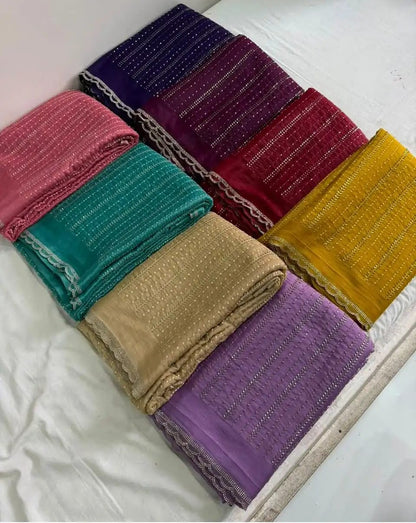 Six folded fabric pieces in pink, teal, beige, purple, dark purple, and mustard yellow, arranged on a white surface. Each fabric has a textured woven pattern with small metallic embellishments and a decorative lace-like border.
