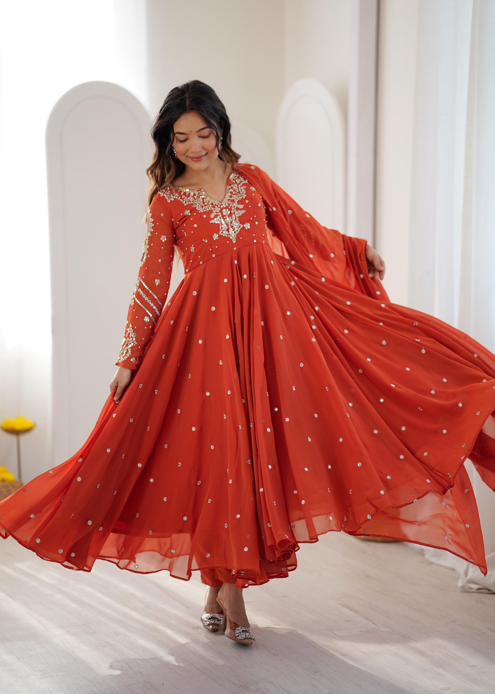 Model twirling in a rust orange sequin embroidered Anarkali gown with flowing dupatta