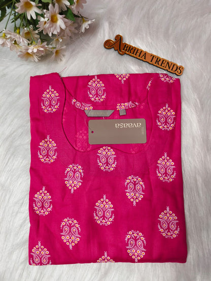 A folded pink kurta with white and gold paisley prints, displayed on a white faux fur surface with a wooden 'Abriha Trends' sign and white daisies in the corner.