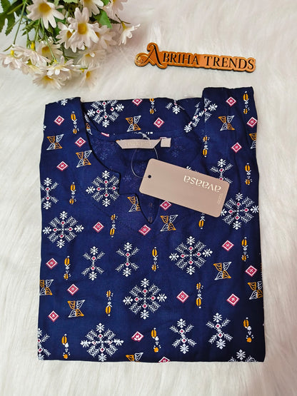 A folded navy blue kurta with a white, pink, and yellow geometric pattern, featuring a beige. The kurta is laid flat on a white faux fur surface next to a wooden 'ABRIHA TRENDS' sign and white daisies.