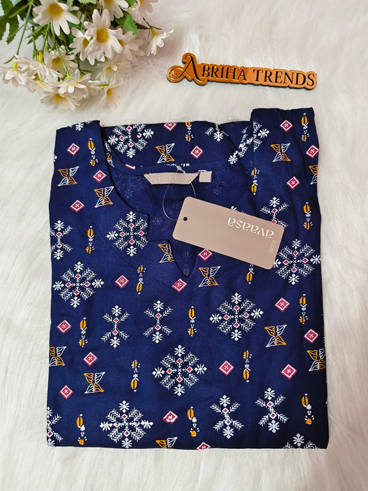 A folded navy blue kurta with a white, pink, and yellow geometric pattern, featuring a beige. The kurta is laid flat on a white faux fur surface next to a wooden 'ABRIHA TRENDS' sign and white daisies.