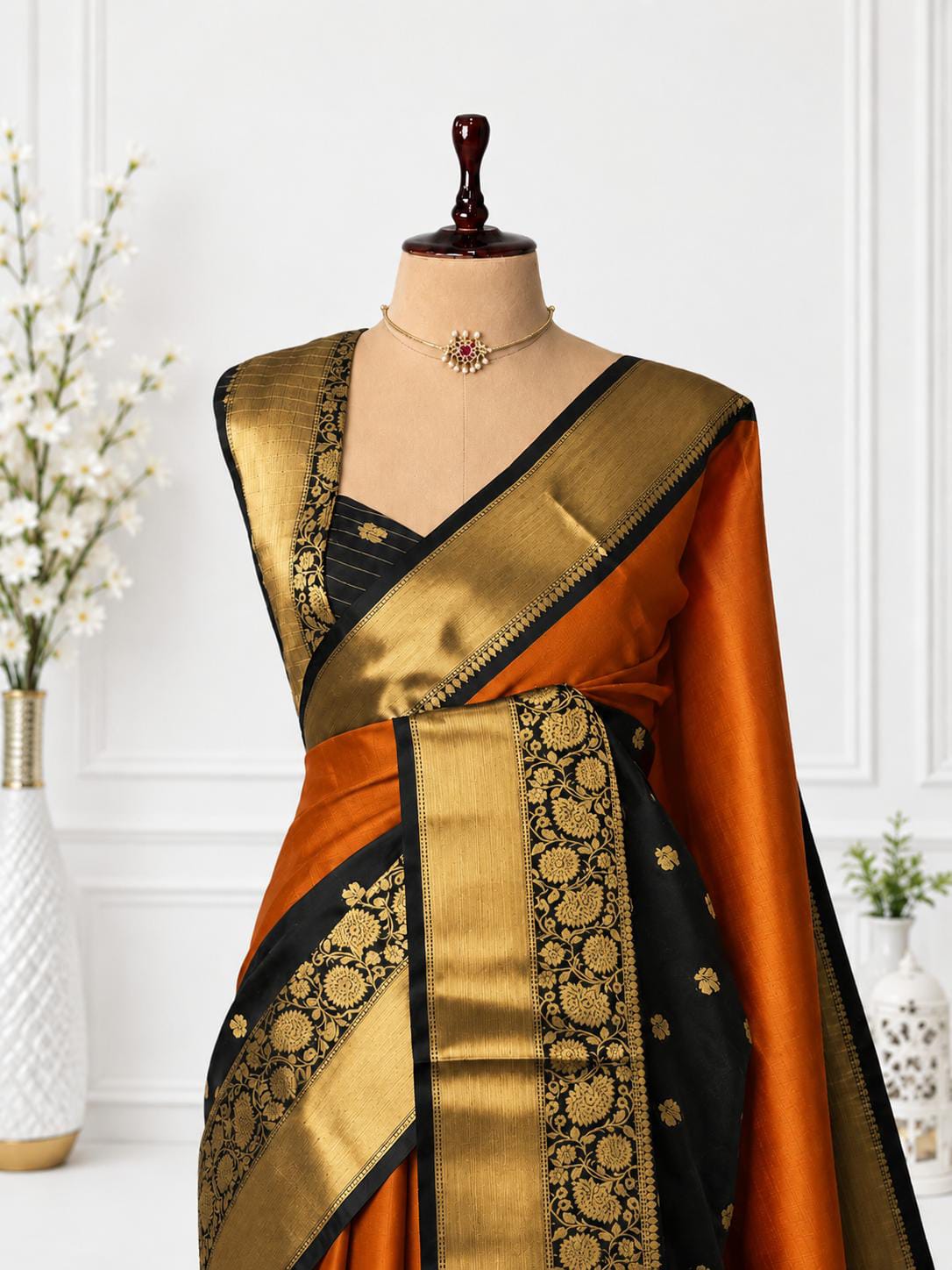 An orange and black silk saree with intricate gold zari brocade work, displayed on a mannequin torso with a matching black blouse.