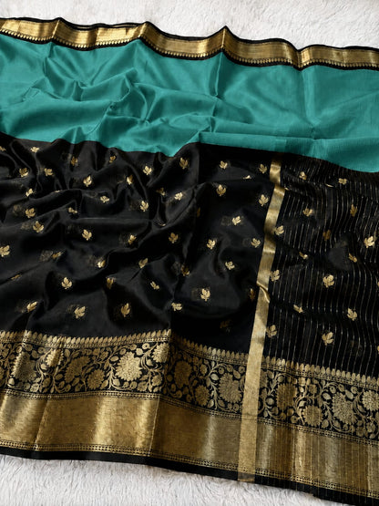 Black and teal green silk saree with intricate gold zari brocade borders and small gold floral motifs, laid flat on a white textured surface.