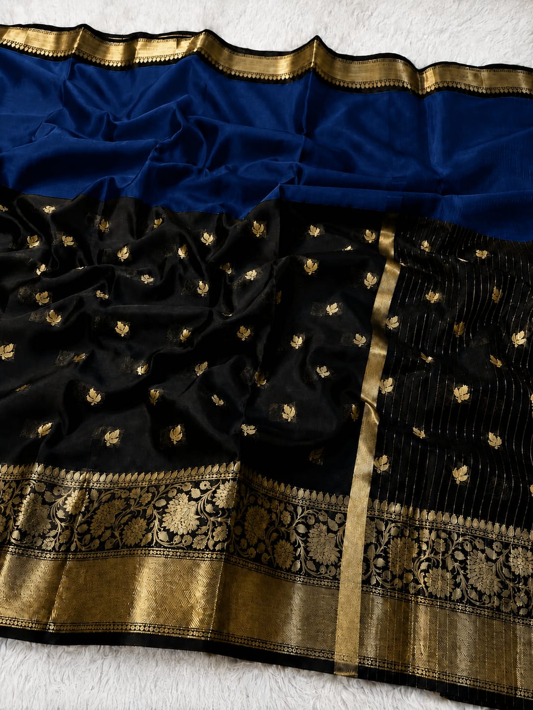 Black silk Banarasi saree with gold zari embroidery, a wide blue border, and a detailed gold brocade pallu, laid flat on a white textured background.