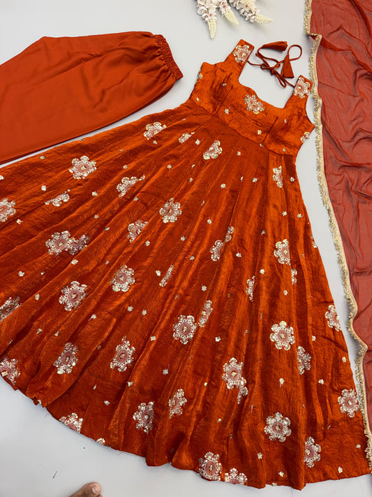 Flat lay of rust Doremon Crush Anarkali gown with palazzo bottom and sheer dupatta, allover gold and white sequin floral embroidery