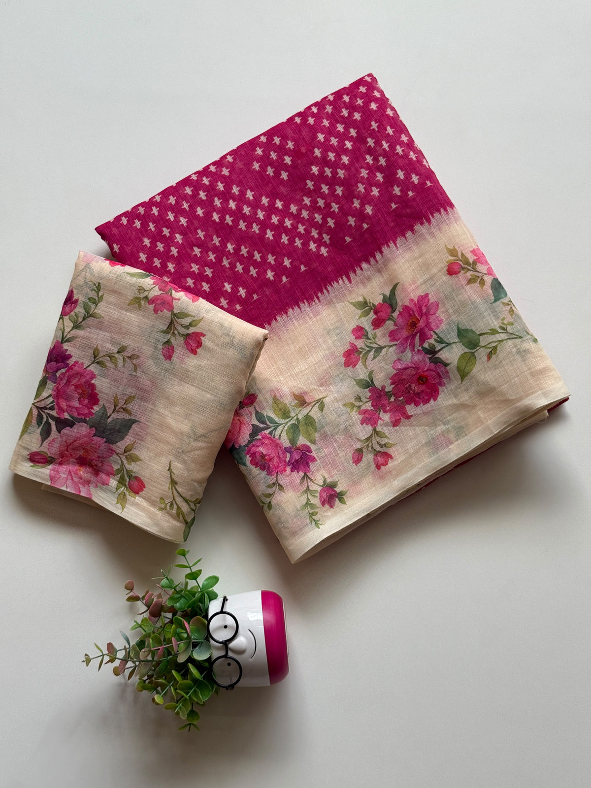 Rani pink linen cotton saree with white cross-motif print and floral digital print border, folded with printed blouse piece