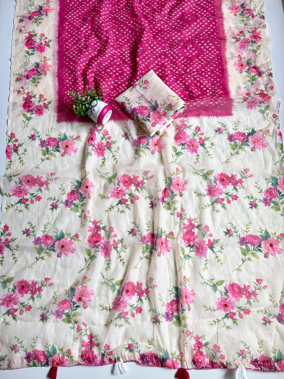 Rani pink linen cotton saree spread out showing cream floral pallu with mirror work and red and white tassels