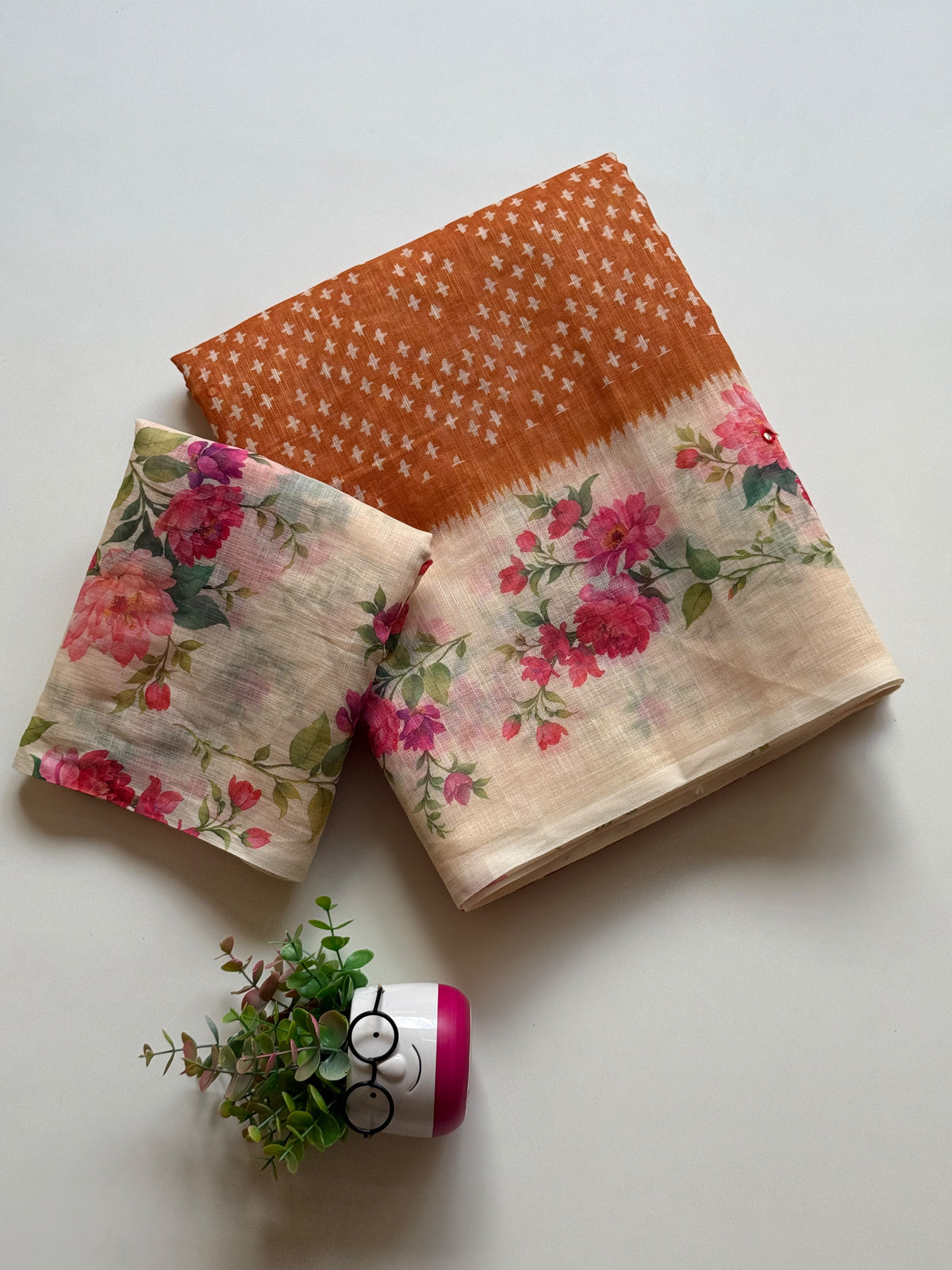 Rust orange linen cotton saree with white cross-motif print and floral digital print border, folded with printed blouse piece