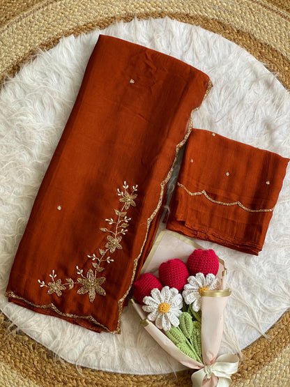 Rust crush silk saree folded with blouse piece, gold bead and pearl floral handwork on the pallu and scalloped bead border