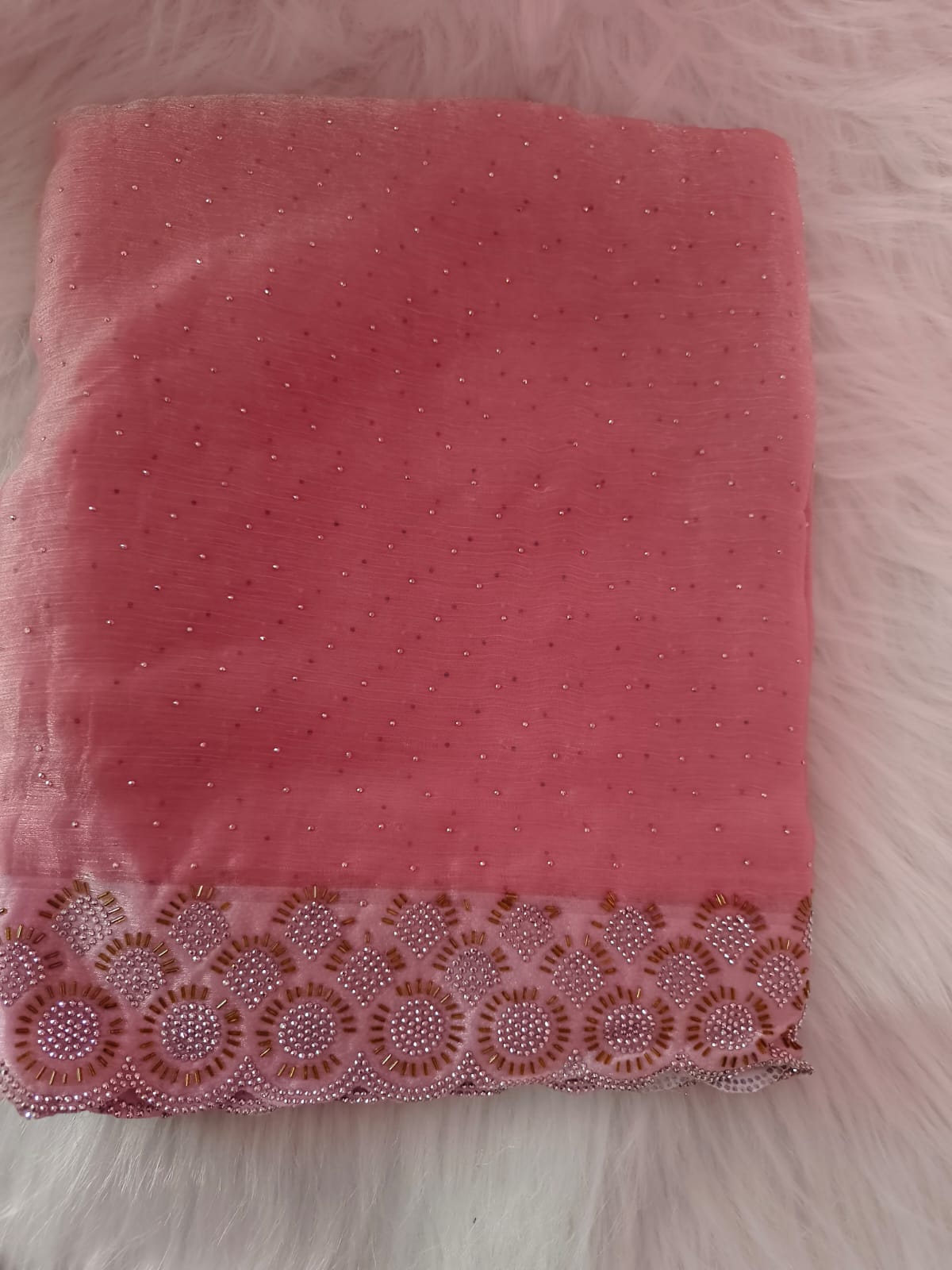 Folded pink space silk saree with small stones across the body and a scalloped stone and bead border