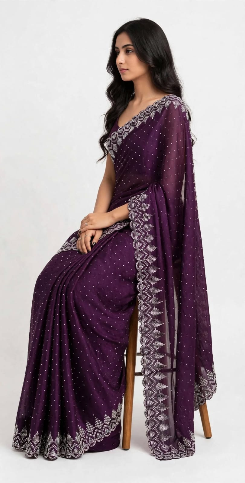 Seated side view of the purple georgette saree with stone dots across the body and the pallu flowing down