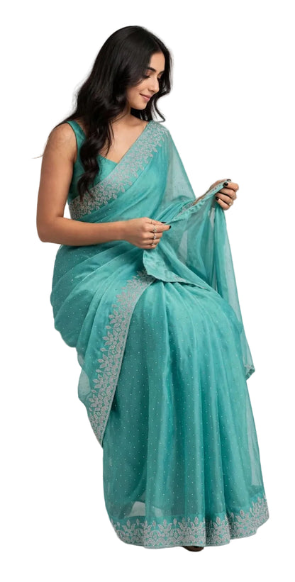 Seated model in the teal space silk saree, showing the stone dotted body and leaf vine border along the pleats