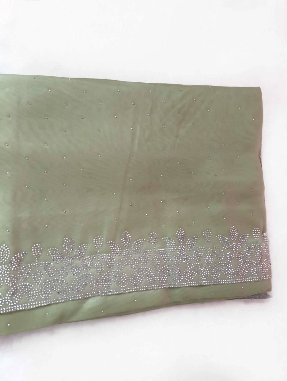 Folded sage green saree showing scattered silver stones and the floral leaf stone border