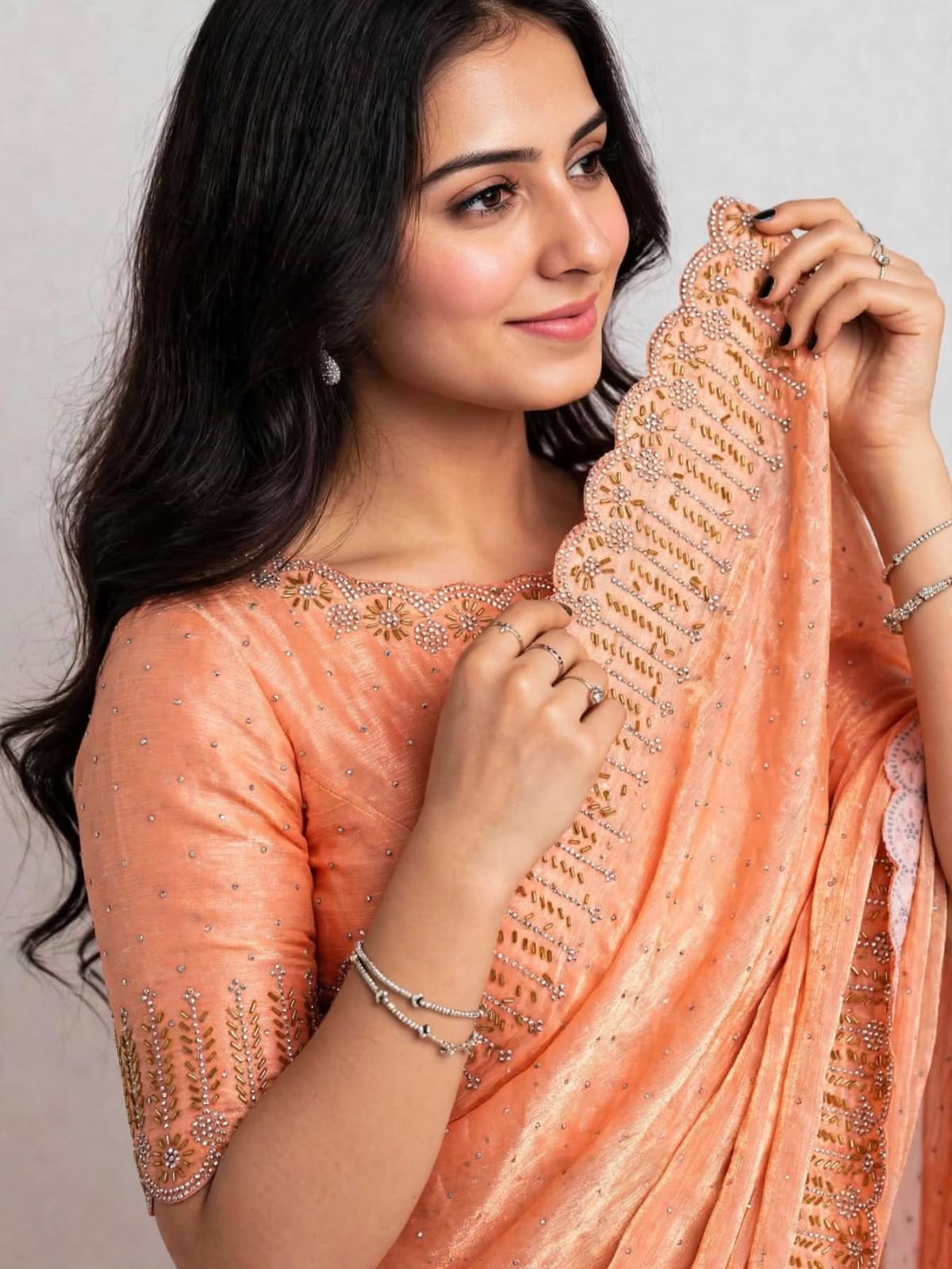 Close-up of the orange saree pallu held up, showing stone flower medallions and gold-tone bead work on the scalloped edge