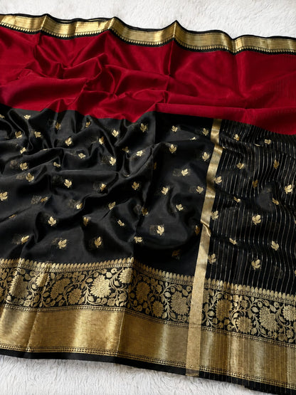 A black silk saree with a rich red pallu, adorned with small gold floral motifs and a wide ornate gold zari border, laid flat on a white textured background.